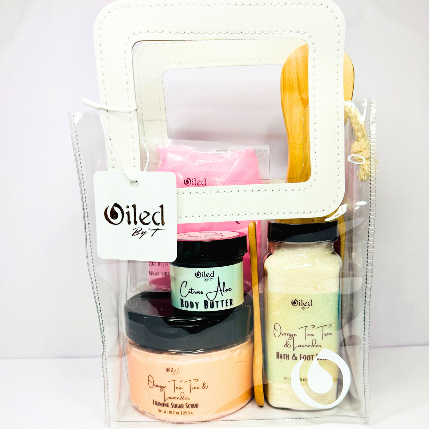 A pedicare set in a clear plastic bag, containing various foot care products including a sugar scrub, body butter, foot soak, silicone socks, and a wooden file.