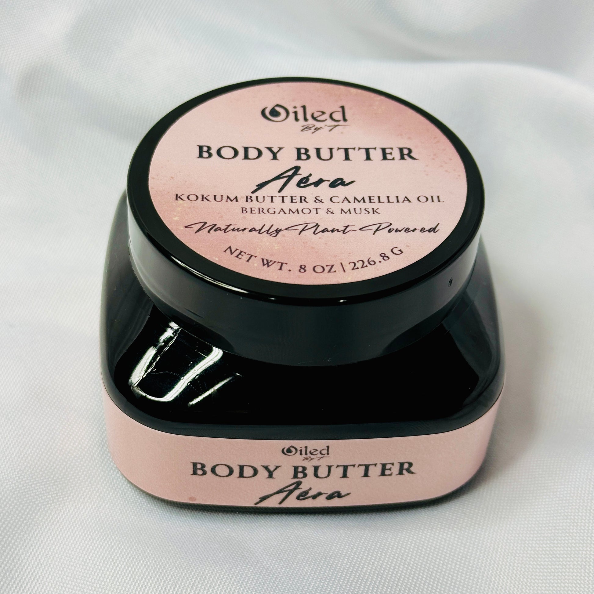Body butter container with pink and black label on a white background